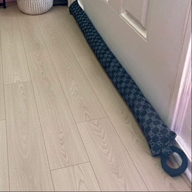Entryway with a white door, wooden floor, and a black Gucci print draft stopper hanging from door knob